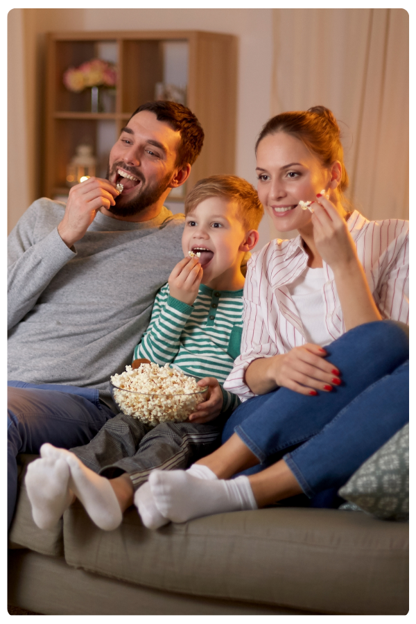 Mother, father, and child sitting on couch eating popcorn and watching TV