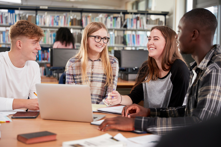 Photograph of high-school aged students sitting around a table. There is a laptop open on the table.